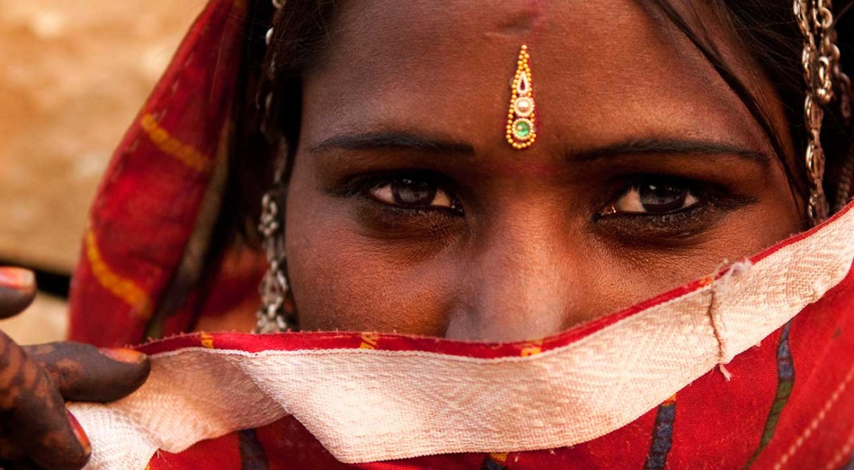 A woman in a red sari covering her face.