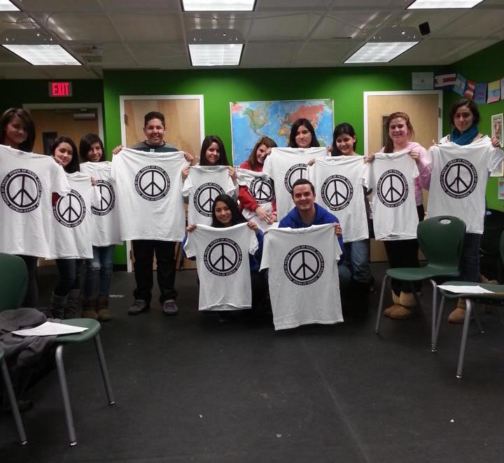 A group of people holding peace sign t - shirts in a classroom.