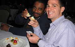 Two men sitting at a table eating desserts.