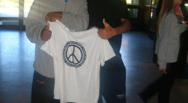 Two young men standing next to each other holding a peace sign t - shirt.