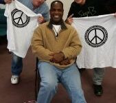 Here's a short alt tag for the image: Three men smiling, holding peace shirts.