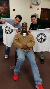 Here's a short alt tag for the image: Three men smiling, holding peace shirts.