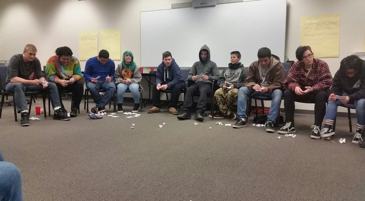A group of people sitting in a room with paper on the floor.