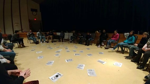 A group of people sitting in a circle with papers on the floor.
