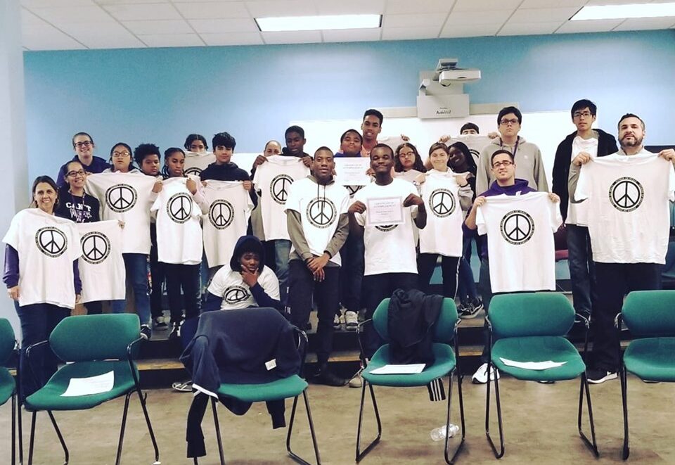 A group of people holding up t - shirts in a classroom.